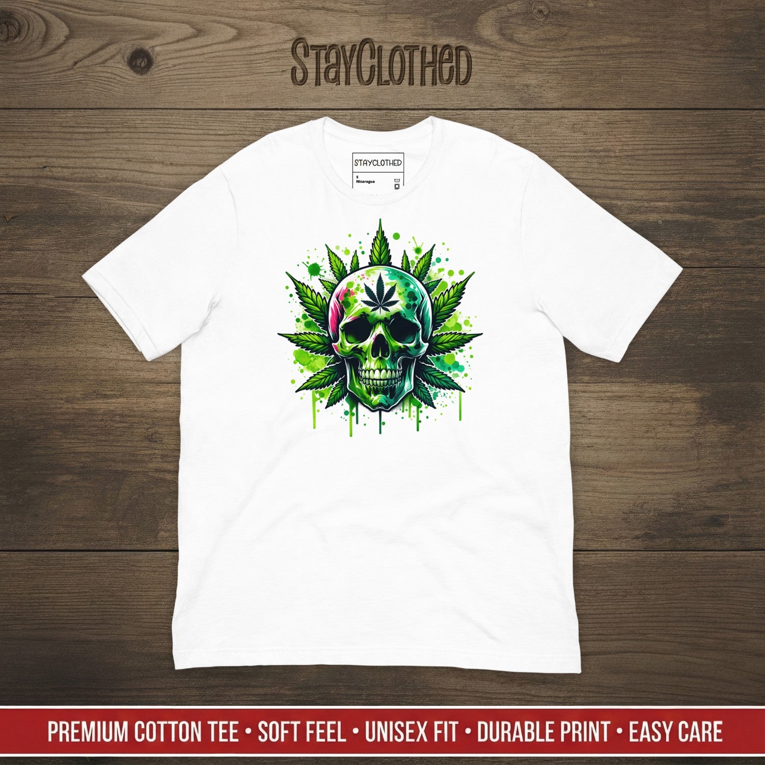 White t-shirt with a colorful skull and cannabis leaf design on a wooden surface, featuring the brand 'StayClothed'.