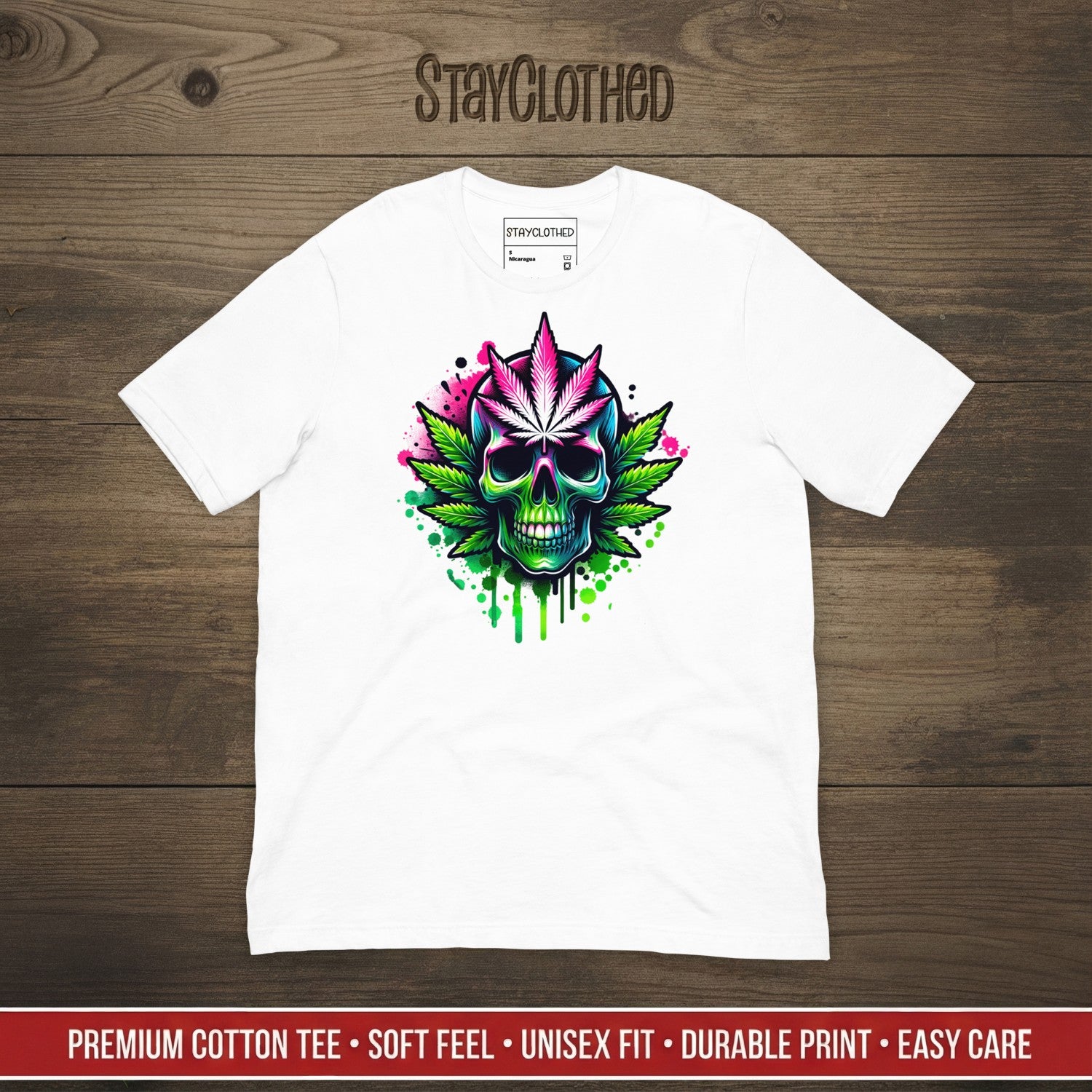 White t-shirt with colorful skull and cannabis leaf design on a wooden surface, featuring the brand 'StayClothed'.