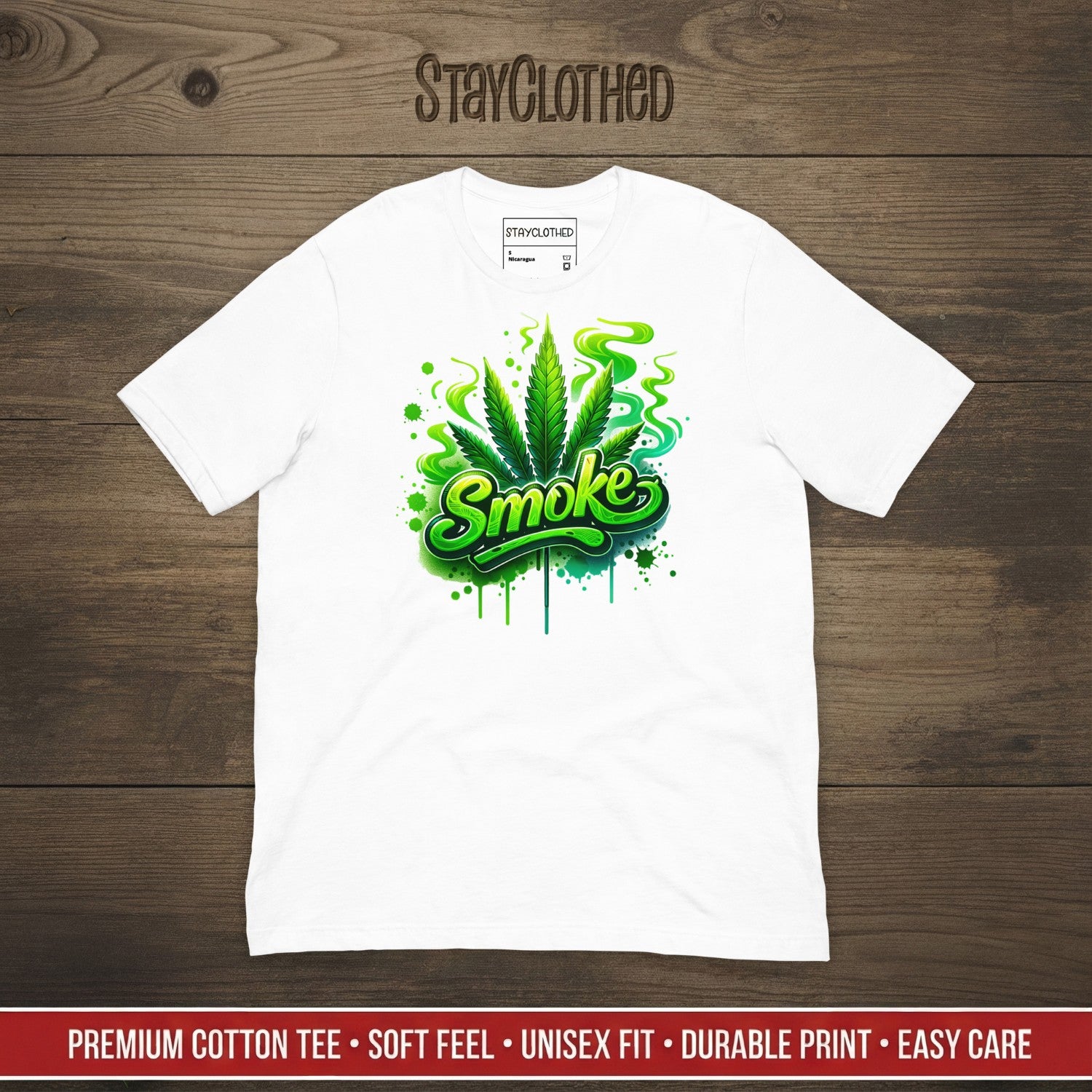 White t-shirt with green 'Smoke' graphic on a wooden surface, featuring 'StayClothed' brand.