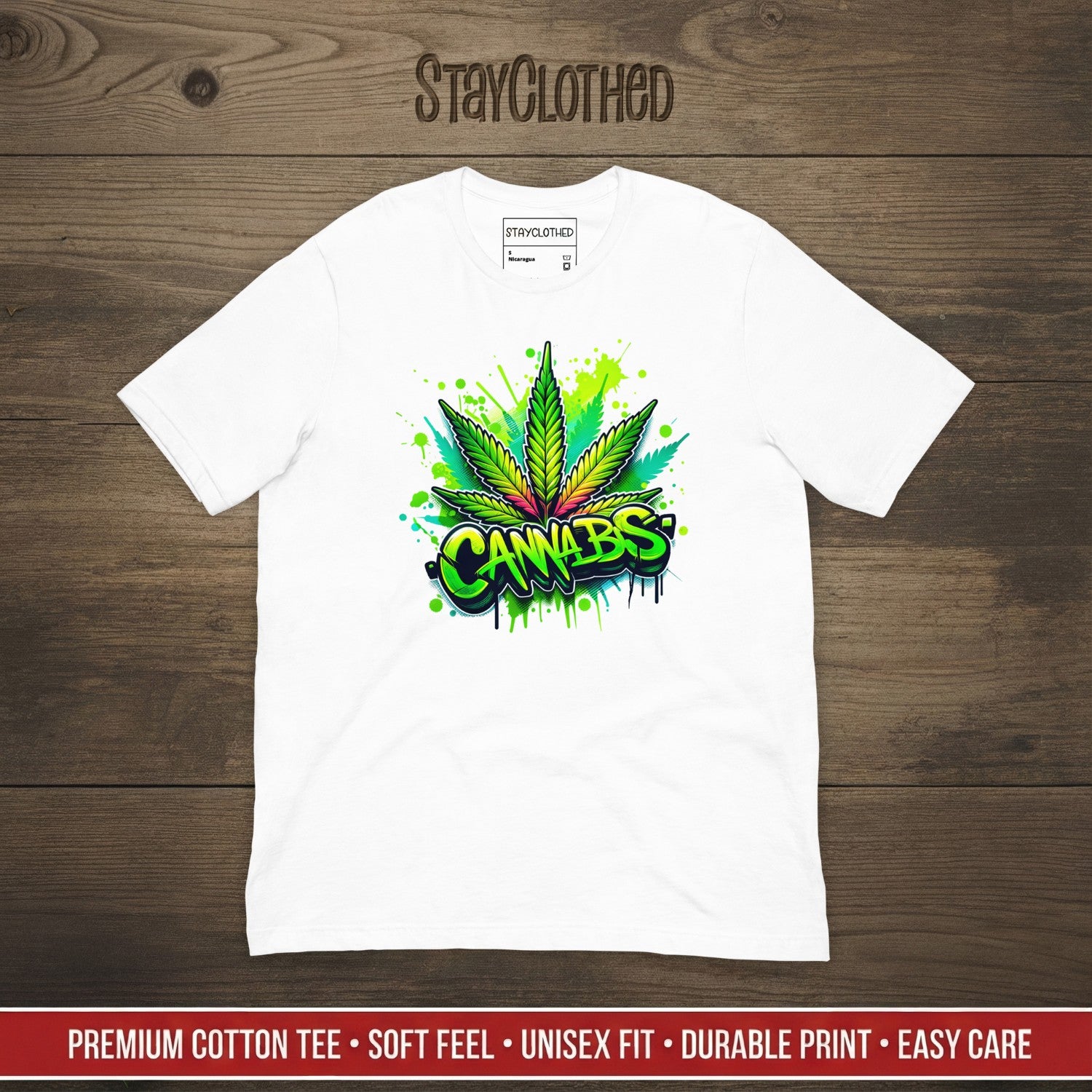 White t-shirt with cannabis leaf graphic on a wooden surface, featuring 'StayClothed' brand.