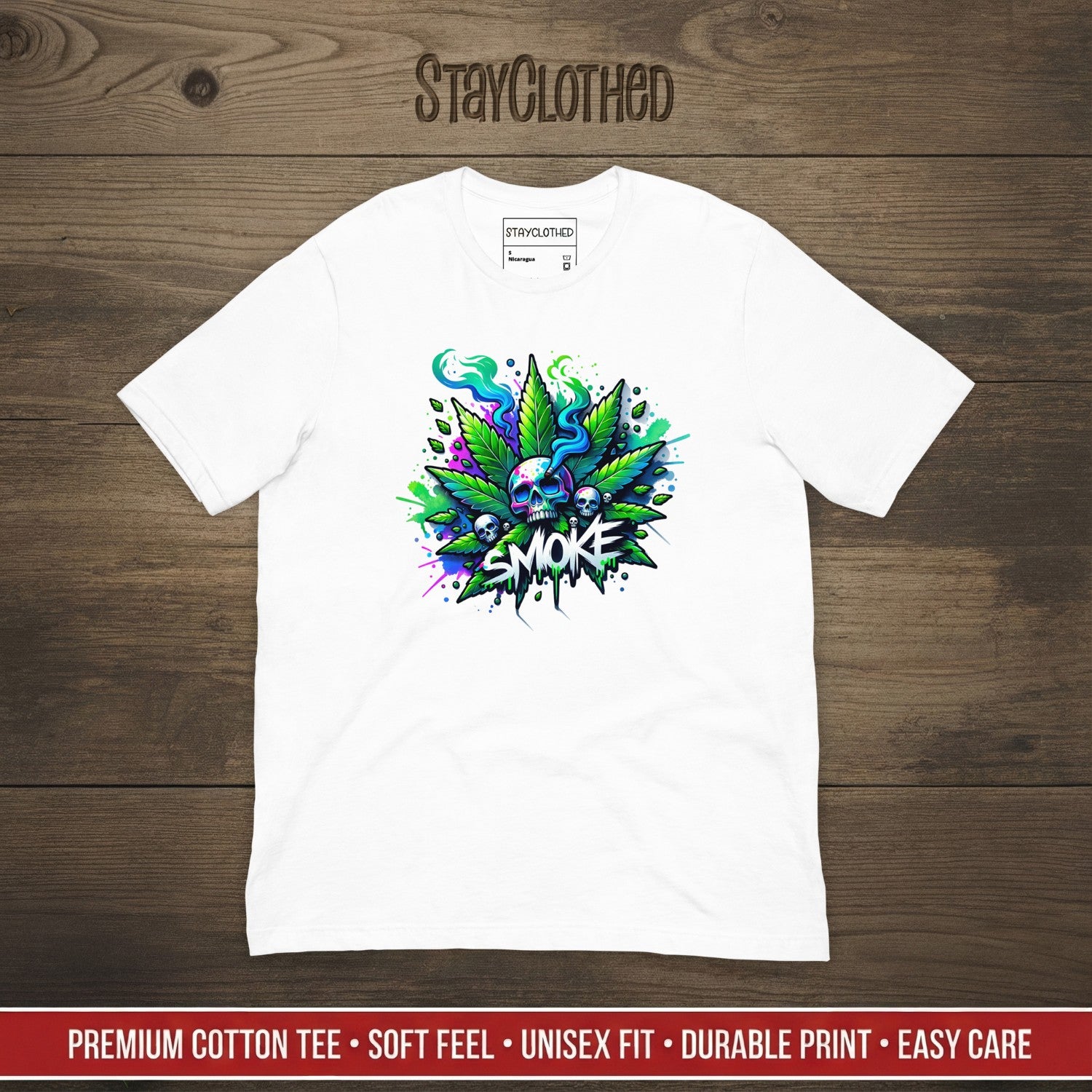 White t-shirt with colorful cannabis leaf design and 'SMOKE' text on a wooden surface, featuring the brand 'StayClothed'.