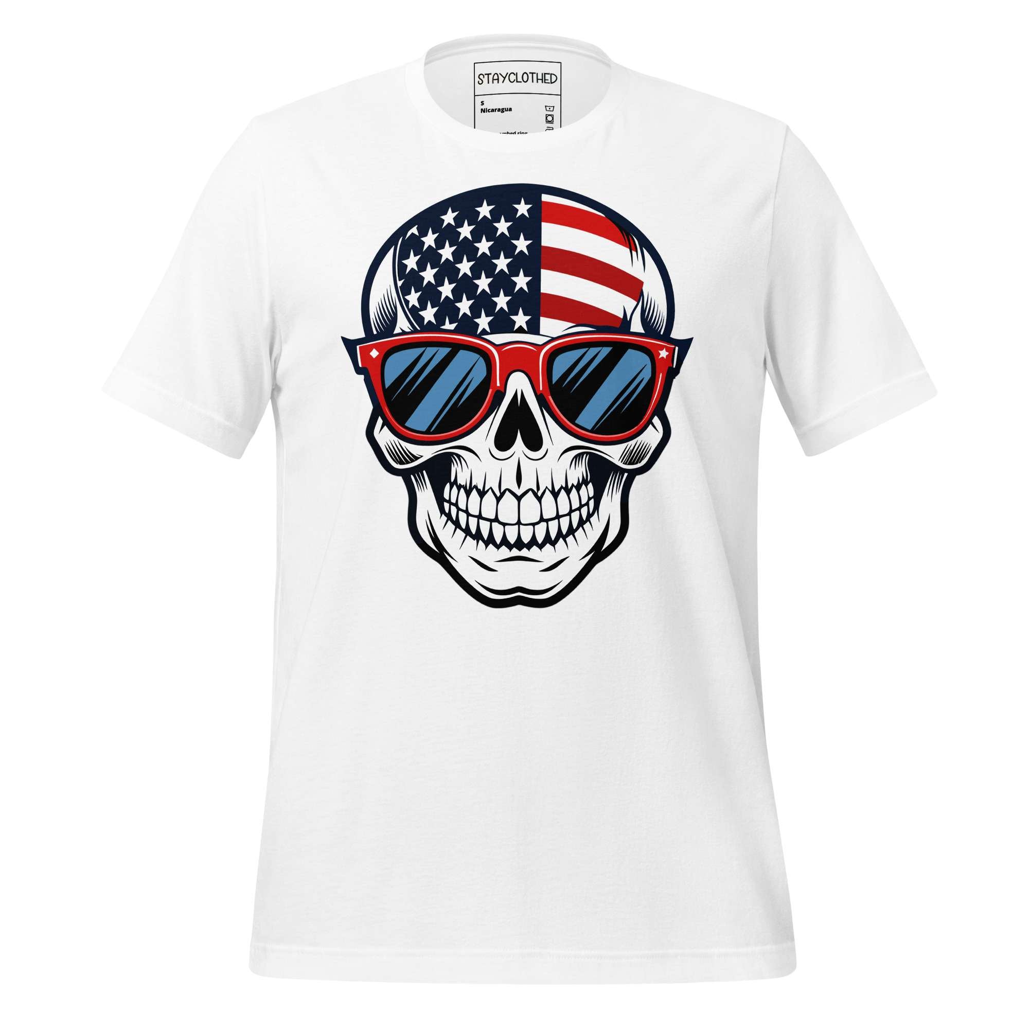 White t-shirt with a skull design wearing American flag sunglasses on a wooden surface, featuring the brand 'StayClothed'.