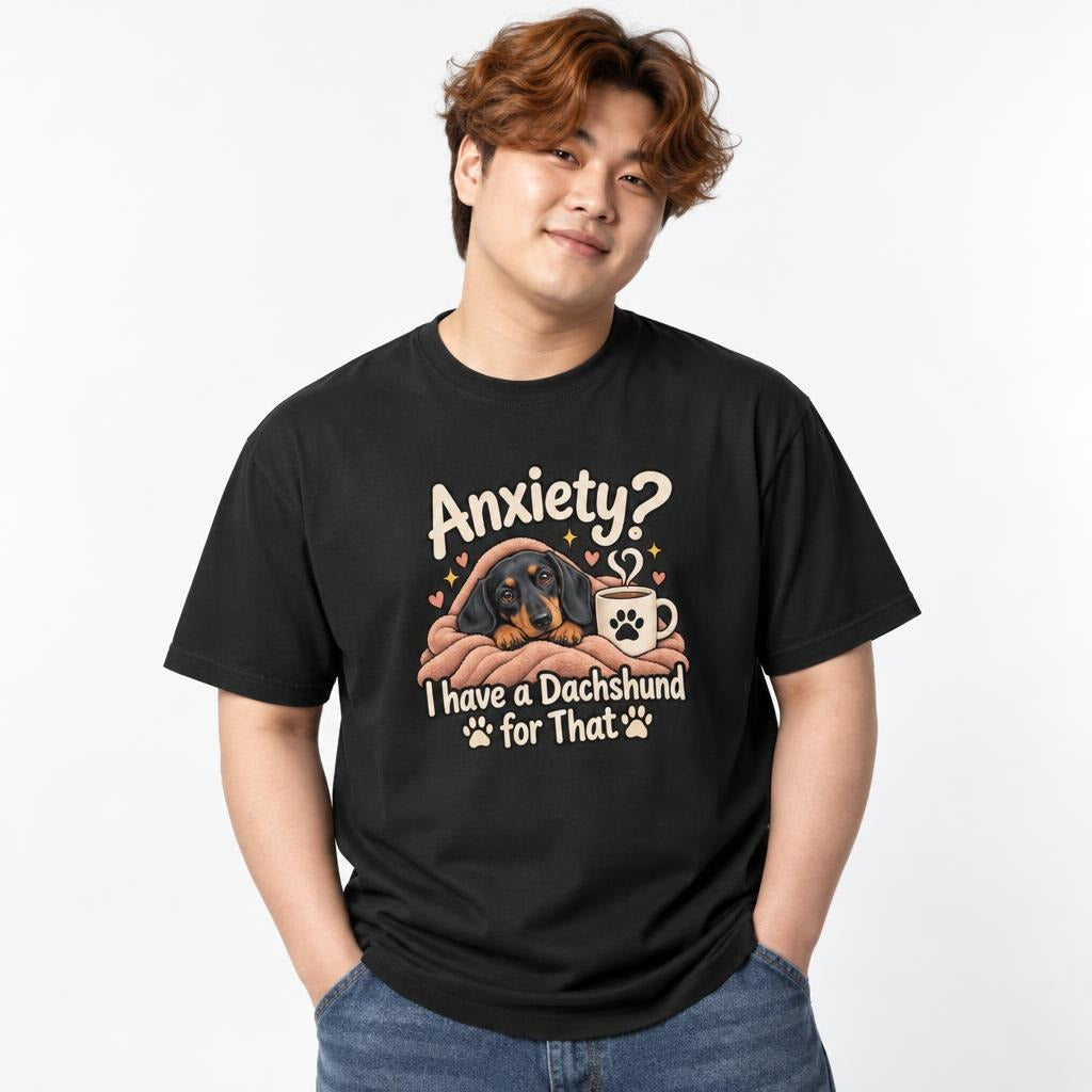 Model wearing a black T-shirt with “Anxiety?” text above a cosy dachshund wrapped in a blanket beside a coffee mug.