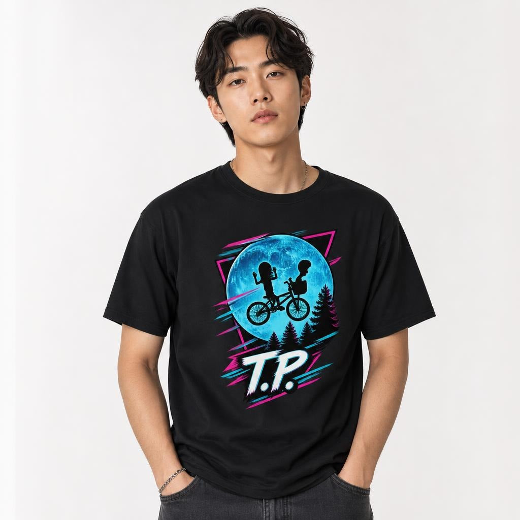 Front view of a black T-shirt featuring two children riding a bicycle against a large blue moon with pine trees and neon accents.