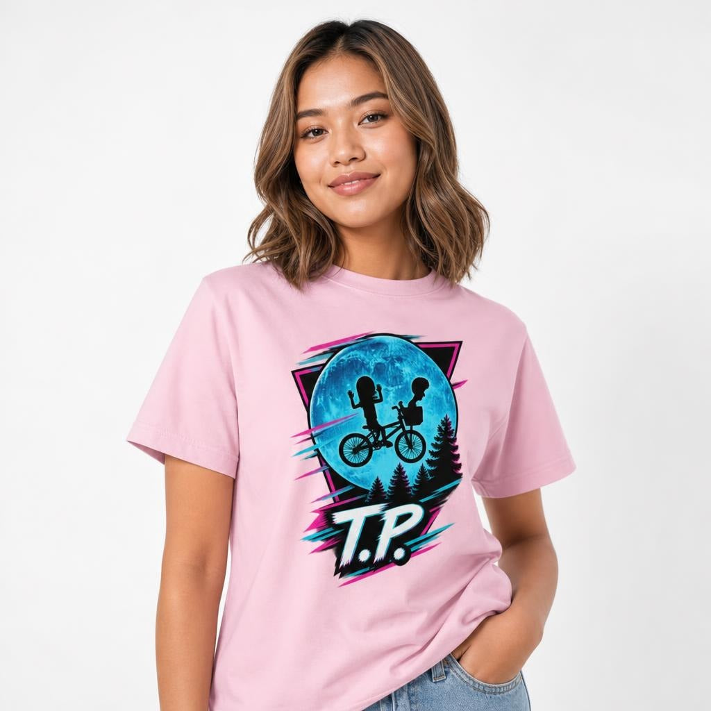 Model wearing a Blossom T-shirt with two children riding a bicycle before a blue moon, pine trees and “T.P.” lettering.