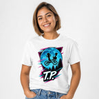 Front view of a white T-shirt featuring two children riding a bicycle against a large blue moon, pine trees, neon accents, and T.P. lettering.