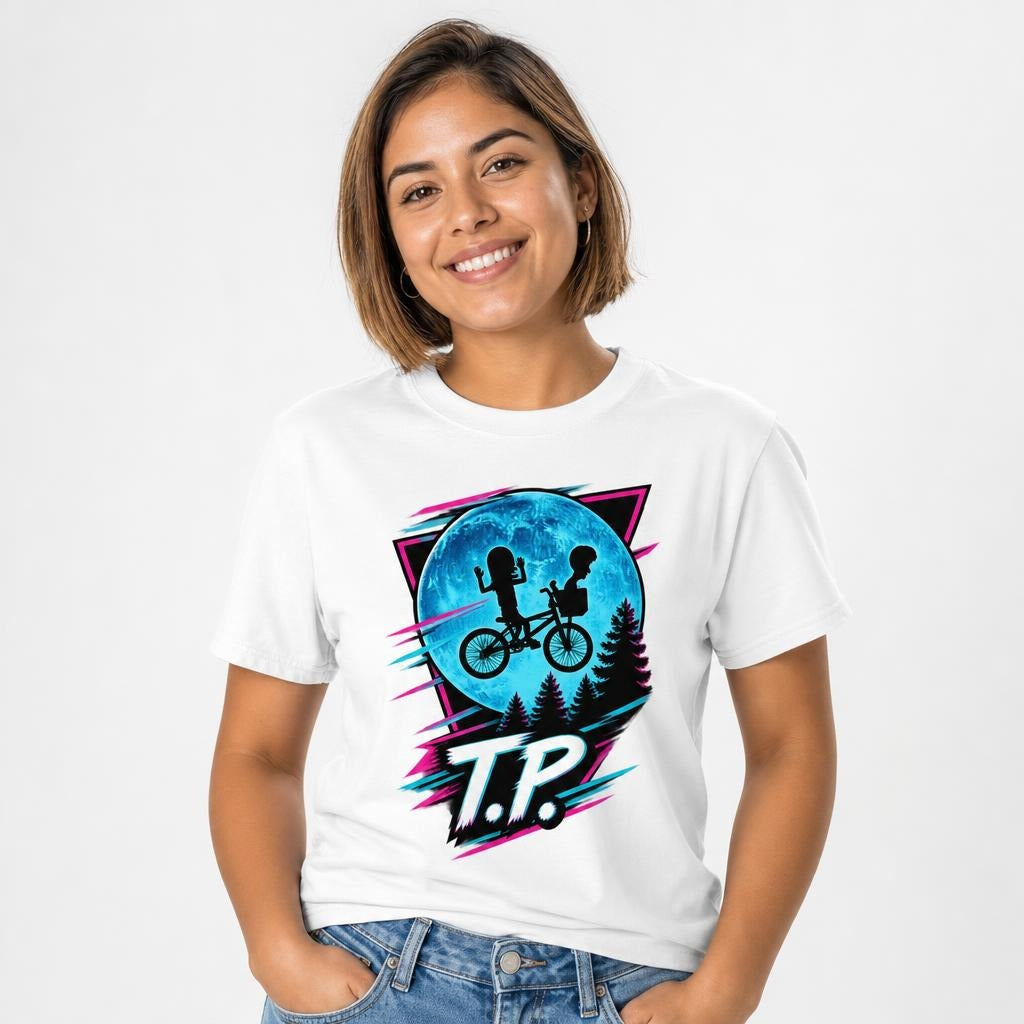 Front view of a white T-shirt featuring two children riding a bicycle against a large blue moon, pine trees, neon accents, and T.P. lettering.
