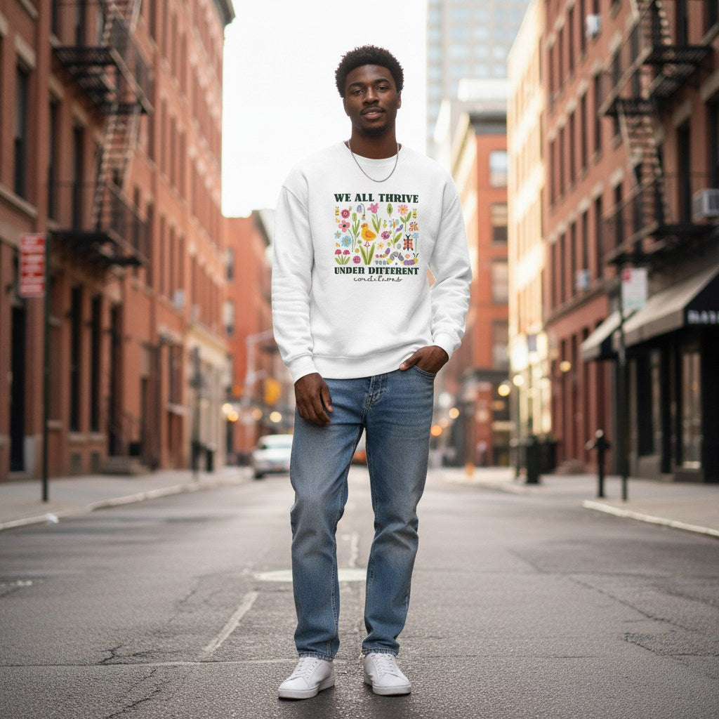 Black man wearing a white "We All Thrive Under Different Conditions" autism awareness sweatshirt.