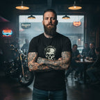 Man with tattoos standing in a bar with neon signs and motorcycles, wearing a black t-shirt featuring a grim dark skull.