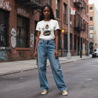 Streetwear shot of a Black woman in a white t-shirt and blue jeans, standing in an urban setting.