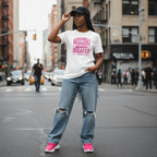 Black woman with an afro hairstyle and trendy streetwear leaning against a white brick wall in a relaxed, confident pose.