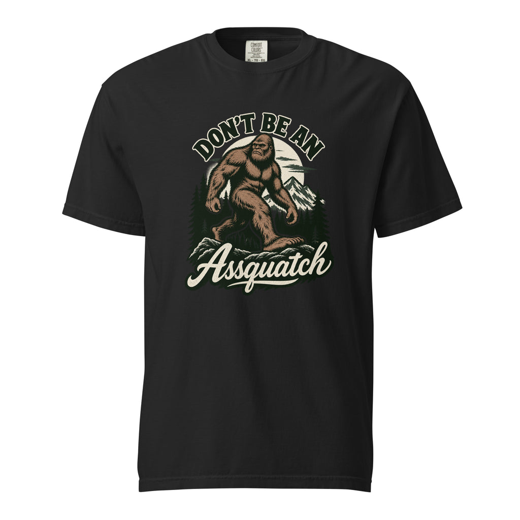Front view of a black T-shirt featuring a vintage-style Sasquatch walking through mountains and pine trees, with “DON’T BE AN” and “Assquatch” text.
