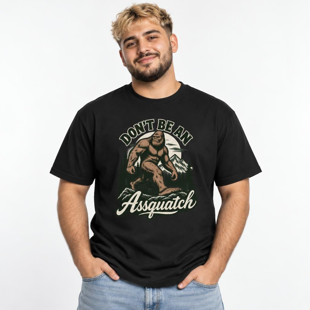 Model wearing a black T-shirt with a vintage-style Sasquatch walking through mountains and pine trees, with “DON’T BE AN Assquatch” text.