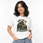 Front view of a person wearing a White T-shirt with a vintage-style Sasquatch among mountains and pine trees, plus “DON’T BE AN Assquatch” text.