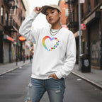 East Asian non-binary person wearing a white rainbow heart puzzle sweatshirt with a small design.
