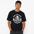 Model wearing a black front-view T-shirt featuring a Bigfoot graphic among mountains beneath a moon.