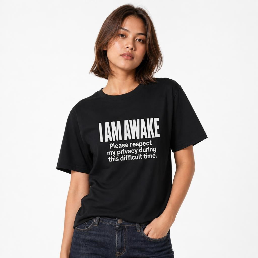 Black t shirt featuring Minimal black-and-white typographic artwork reading “I AM AWAKE” with the subtext “Please respect my privacy during this difficult time.”, model view