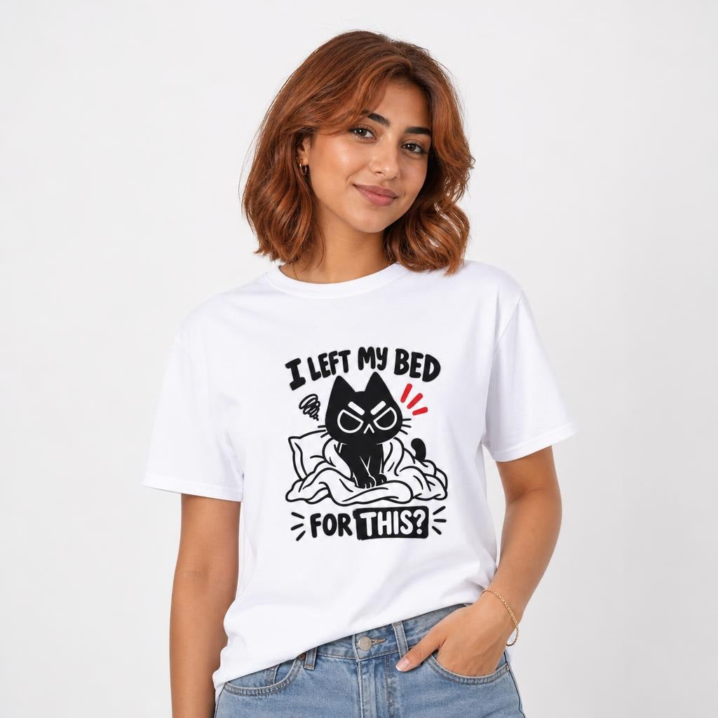 Model wearing a white T-shirt with a grumpy black cartoon cat on a rumpled bed beneath the words “I LEFT MY BED FOR THIS?”