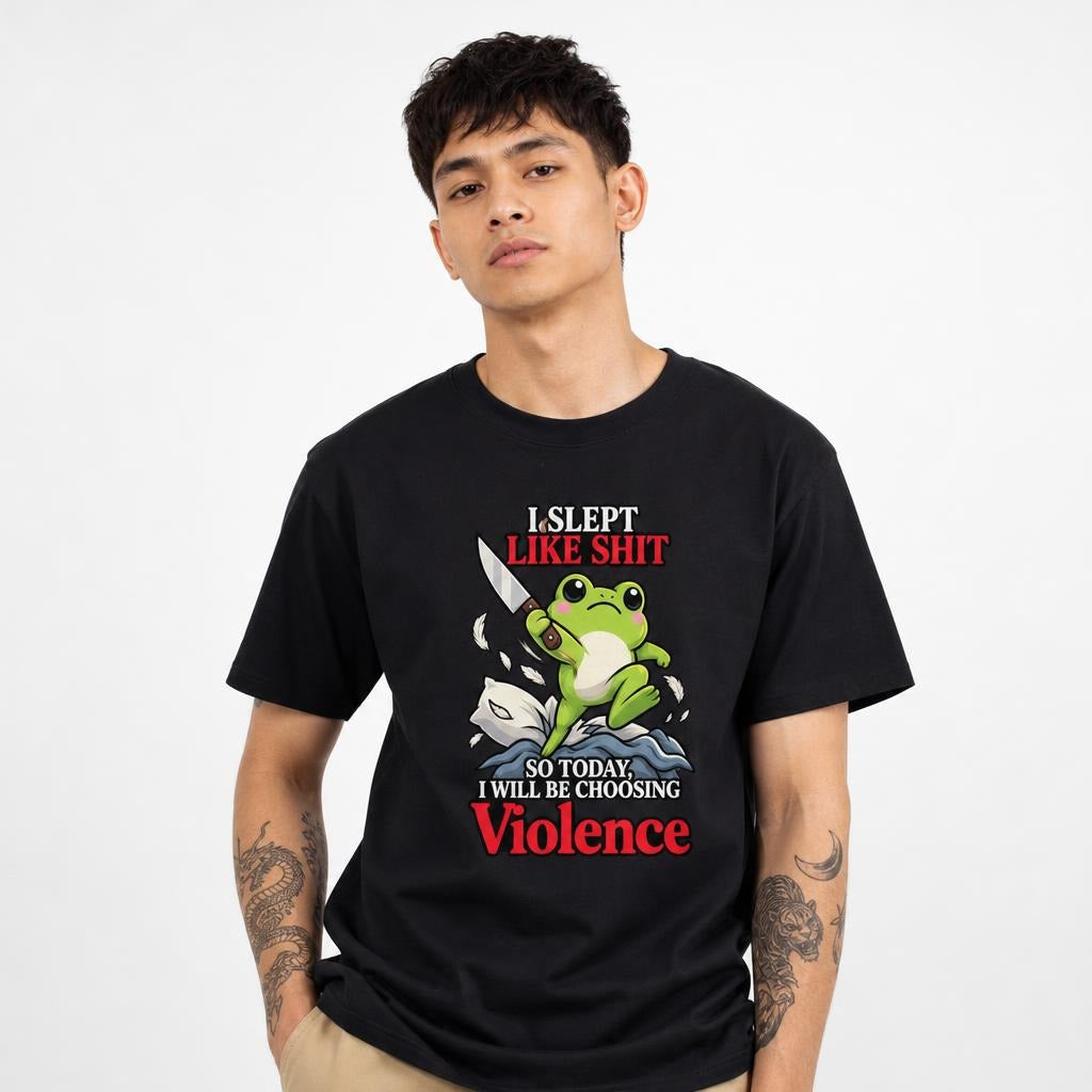 Front view of a black T-shirt featuring a green frog holding a knife above stylized waves, with bold text reading “I SLEPT LIKE SHIT.”