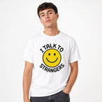 Model wearing a white T-shirt with a yellow smiley face and black “I TALK TO STRANGERS” graphic text.