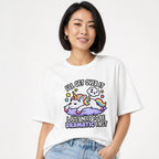 Model wearing a white T-shirt with a colorful cartoon unicorn resting on a purple cloud, stars, rainbow mane, and playful text