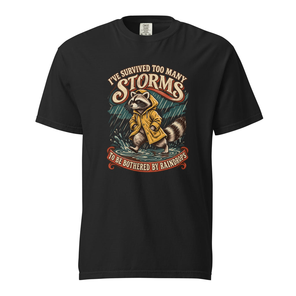 A black T-shirt features a raccoon in a yellow raincoat beneath the words “I’ve survived too many storms” and “to be bothered by raindrops.”