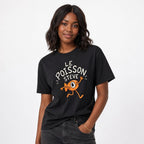 Model wearing a black T-shirt with a humorous orange one-eyed running fish beneath the words “LE POISSON STEVE.”