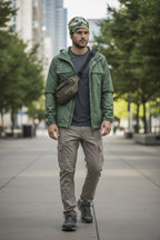 Man wearing a green jacket and pants with a bag, standing on a city street.