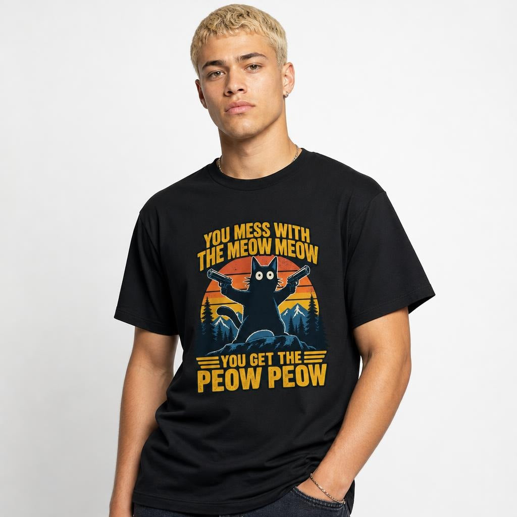 Model wearing a black T-shirt with a cat holding two pistols before mountains, pine trees, and a striped sunset graphic.