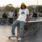 Middle Eastern non-binary person wearing a white be kind autism awareness t-shirt.