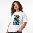 Model wearing a White T-Shirt featuring a bandage-wrapped mummy riding a blue skateboard above bold “STAY BOARDIN’” lettering.