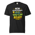 Front view of a black T-shirt featuring “NEW ACHIEVEMENT! YOU CAN READ!” with a yellow trophy, colourful rays, and starbursts.