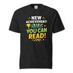 Front view of a black T-shirt featuring “NEW ACHIEVEMENT! YOU CAN READ!” with a yellow trophy, colourful rays, and starbursts.