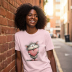 Woman wearing a pink t-shirt with a cartoon cat holding a heart, standing against a brick wall.