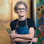 Person wearing a blue apron and glasses with a colorful background