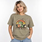 Front view of a Sandstone T-shirt with “Sometimes I Just Be Fartin” lettering, a frog holding a steaming coffee cup, sunset stripes, and trees.
