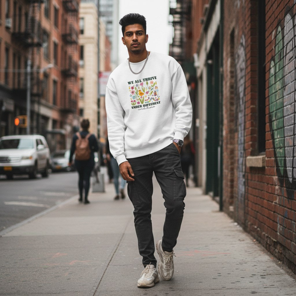 South Asian man wearing a white "We All Thrive Under Different Conditions" autism awareness sweatshirt.