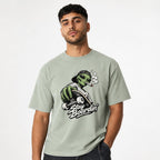Model wearing a Bay T-shirt with a green alien in a backwards cap riding a skateboard, curling smoke and “Stay Boardin’” lettering.
