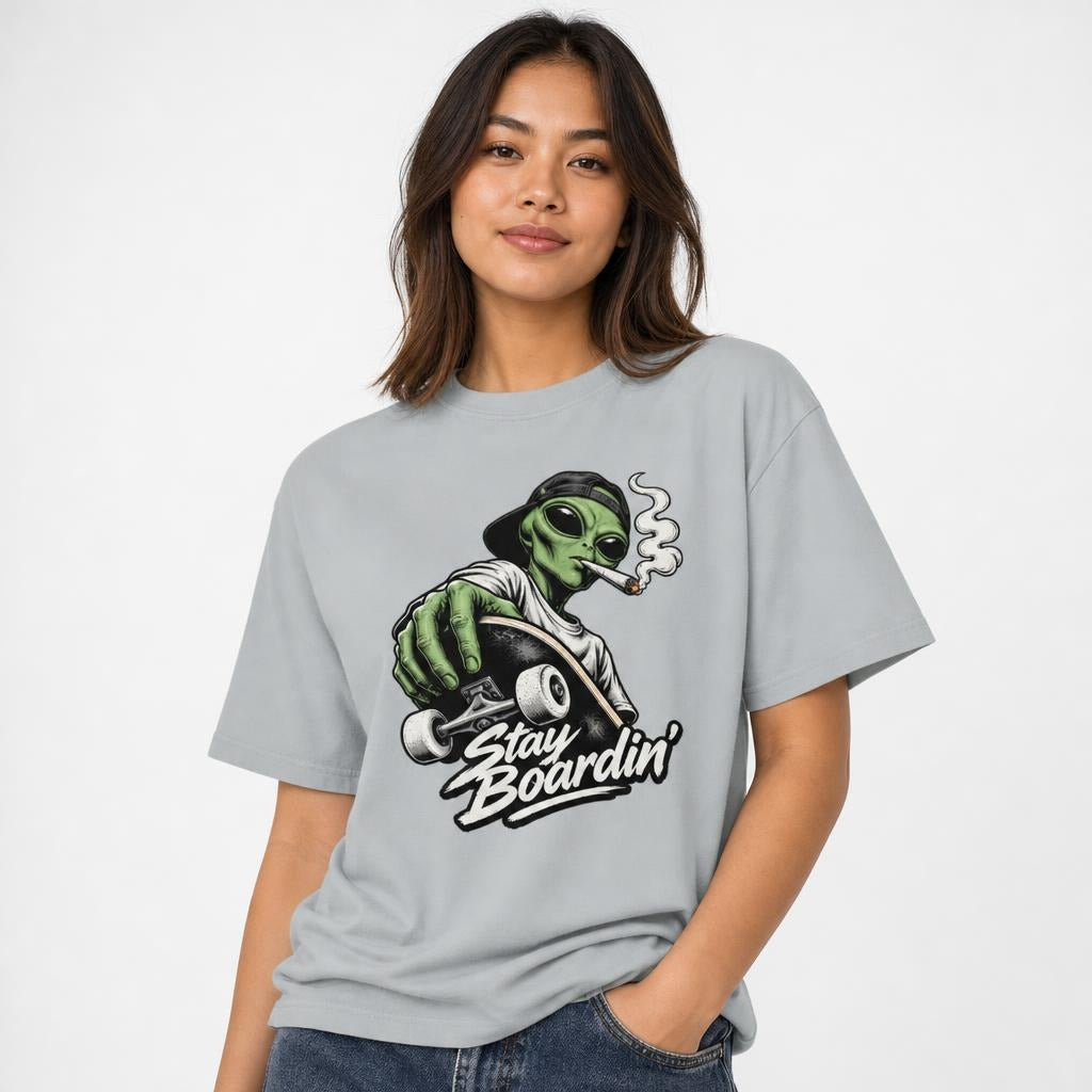 Model wearing a Granite T-Shirt featuring a green alien in a backwards cap riding a skateboard, smoking above “Stay Boardin’” lettering.