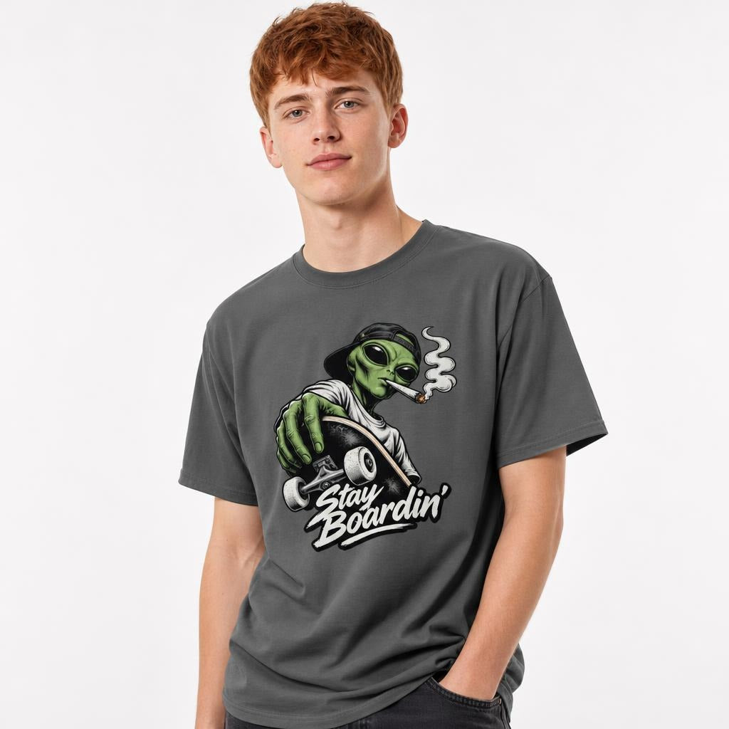 Model wearing a Pepper T-Shirt featuring a green alien in a backwards cap riding a skateboard, with smoke and “Stay Boardin’” lettering.
