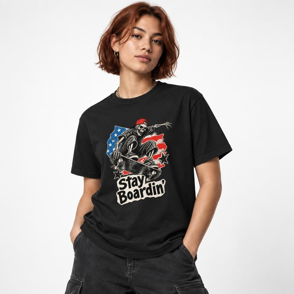 Model wearing a Black T-shirt with a distressed skateboard and skeleton graphic, red, white and blue details, and “Stay Boardin’” text.