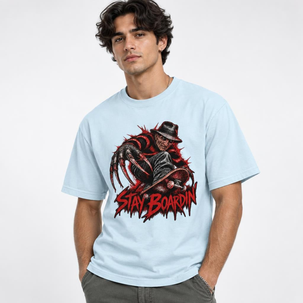Model wearing a Chambray T-shirt with a horror figure, elongated claws, skateboard, and distressed red “STAY BOARDIN’” lettering.