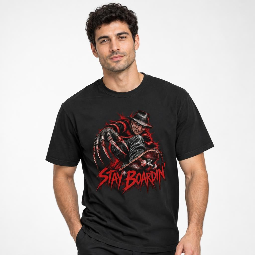 Model wearing a black T-shirt with a horror figure and skateboard graphic, plus distressed red “STAY BOARDIN’” lettering.