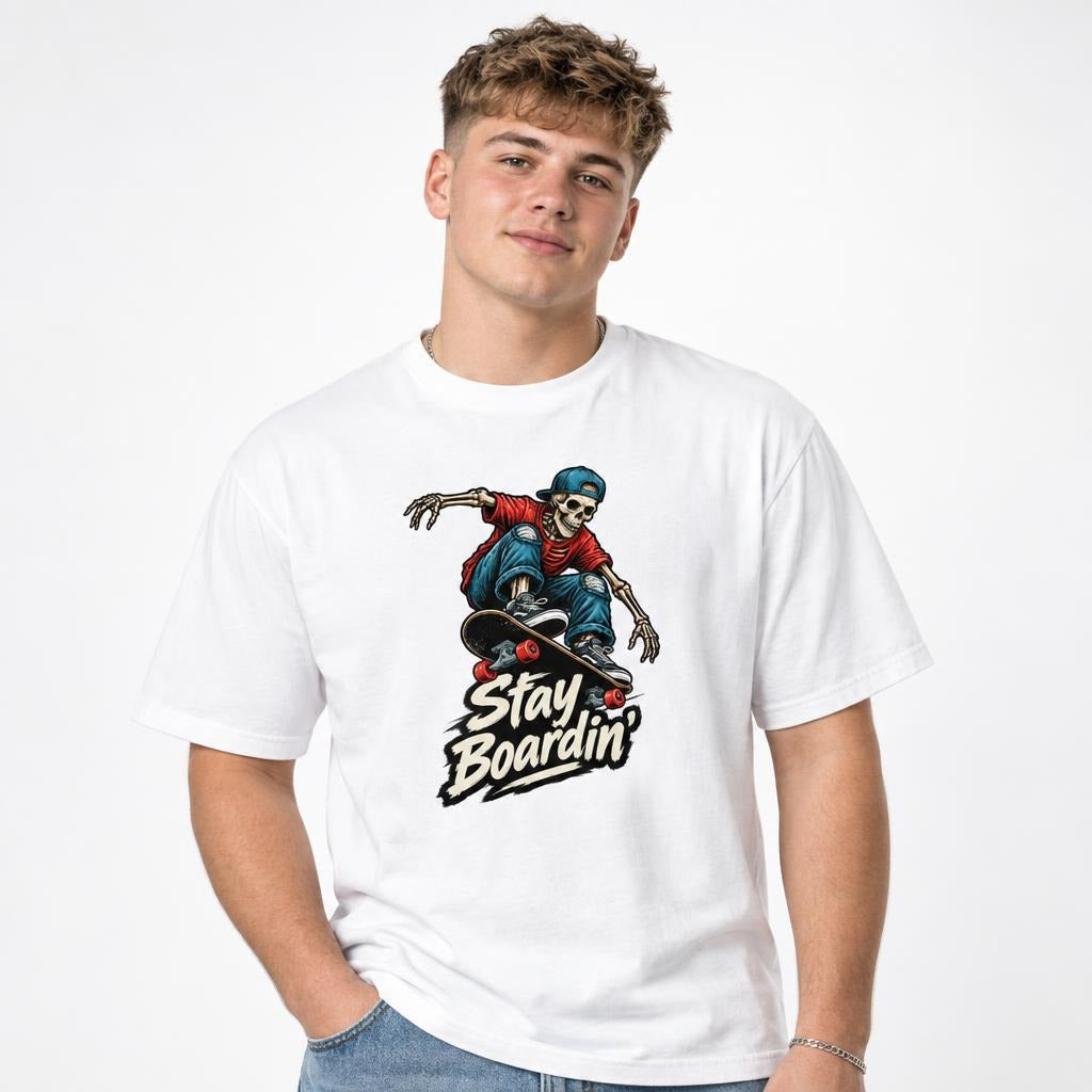 Front view of a white T-shirt with a skeleton in a backwards cap riding a skateboard above “Stay Boardin'” lettering.