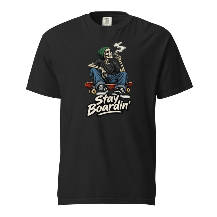 Front view of a black T-shirt with a seated smoking skeleton wearing a green beanie on a skateboard above “Stay Boardin’” lettering.