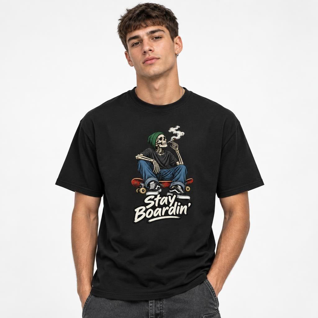 Front view of a model wearing a black T-shirt with a seated smoking skeleton on a skateboard and “Stay Boardin’” lettering.