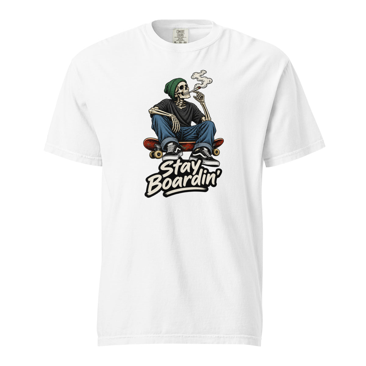 Front of a white T-shirt featuring a seated skeleton in a green beanie smoking on a skateboard above cream “Stay Boardin’” lettering.