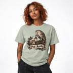 Front view of a Bay T-shirt featuring an owl, skull, and lantern above a scroll reading “Stay Spooky.”