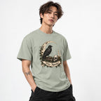 Model wearing a Bay T-shirt with a vintage gothic illustration of a raven, skull, crescent moon, candle, ivy, and “Stay Spooky” scroll.