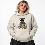 Model wearing an Oatmeal Heather hoodie with a black cat in a witch hat sitting on an orange pumpkin and Stay Spooky lettering.